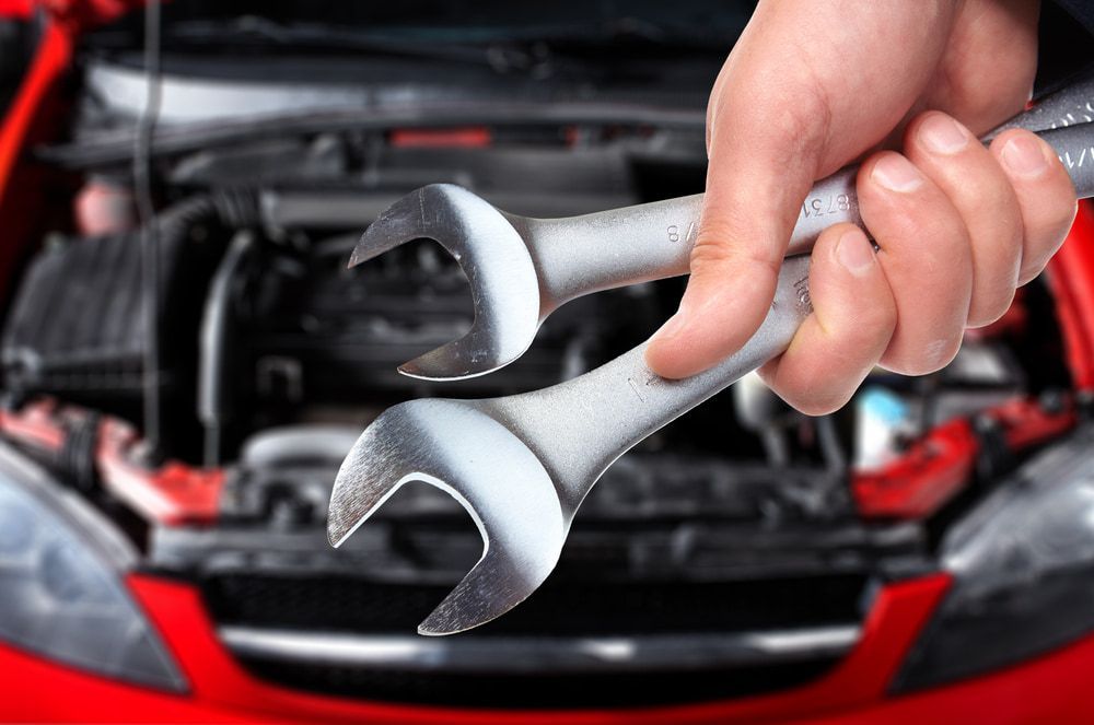 A Person Is Holding Two Wrenches In Front Of A Red Car — Dore's Goodyear Autocare Tully In Tully, QLD