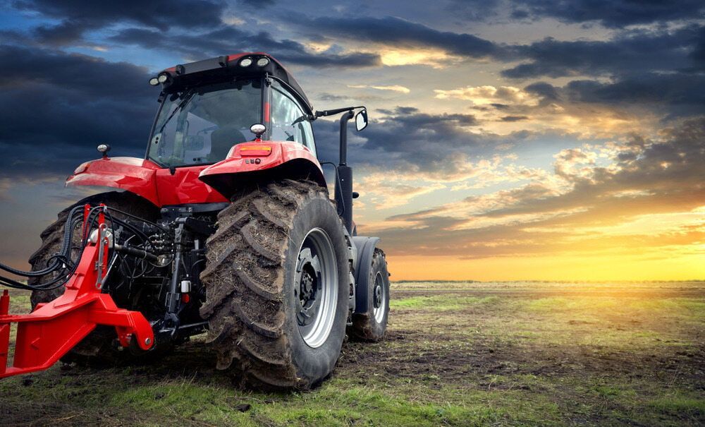 A Red Tractor Is Parked In A Field At Sunset — Dore's Goodyear Autocare Tully In Tully, QLD