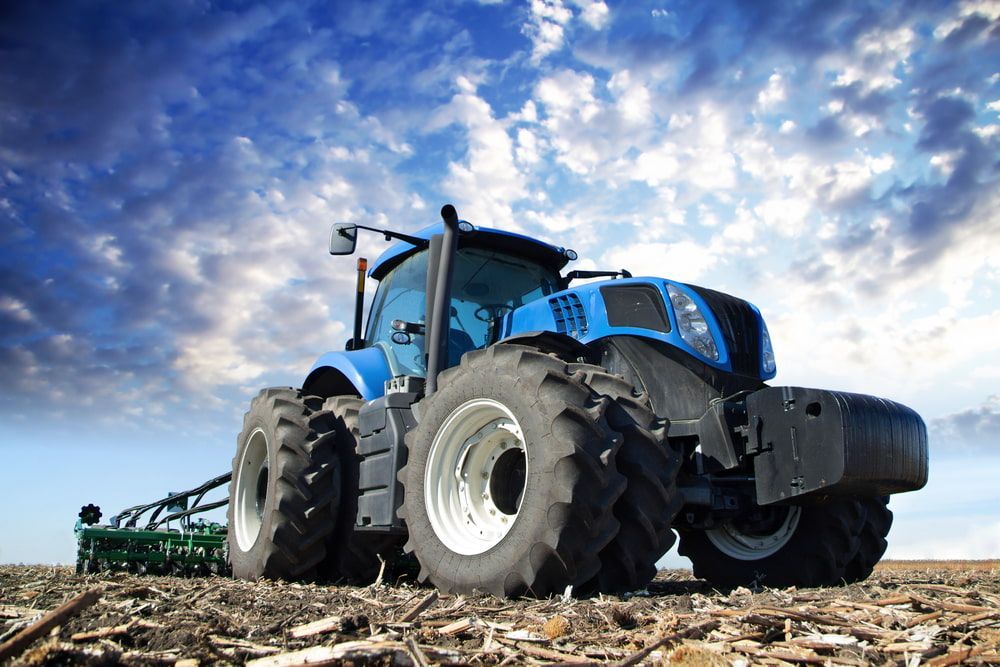 A Blue Tractor Is Plowing A Field With A Plow Attached To It — Dore's Goodyear Autocare Tully In Tully, QLD