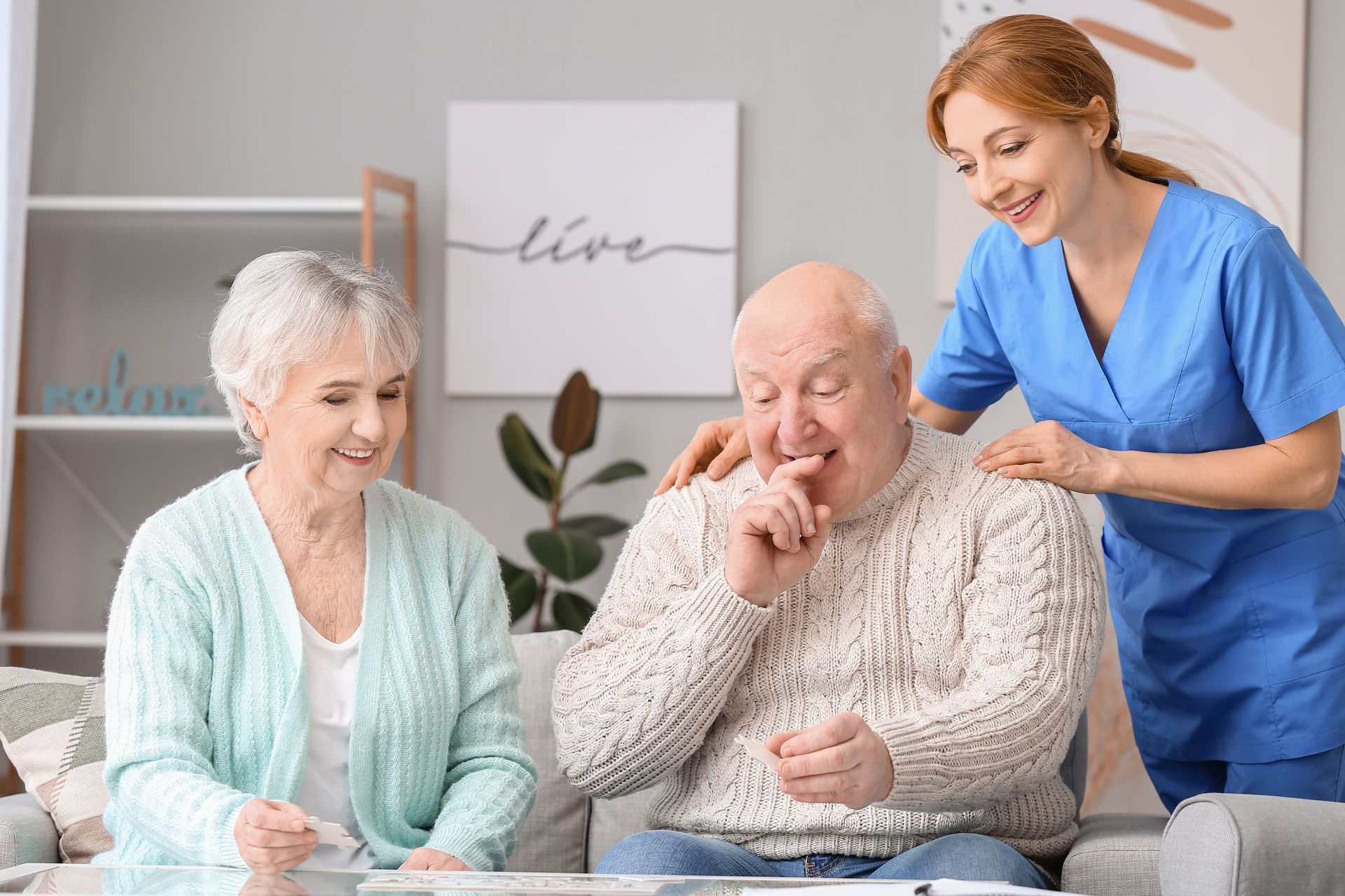 Elderly couple with caregiver; man coughing, woman watches; indoor.