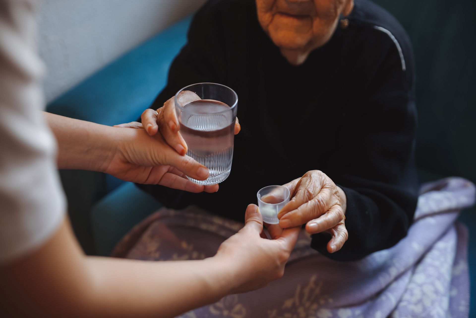 Person holding a glass of water and pill to give to another person sitting on a couch.