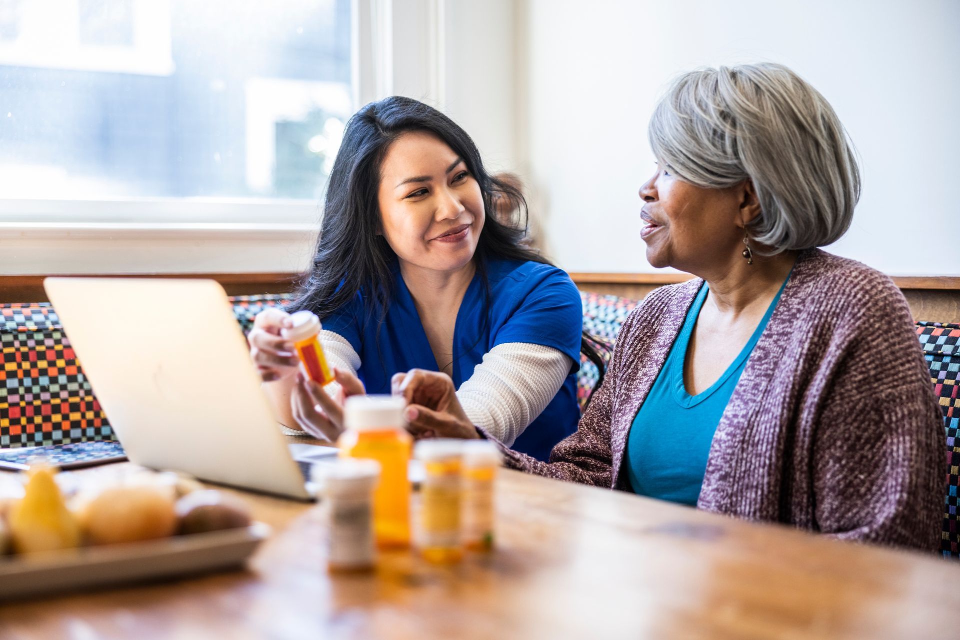 Healthcare worker reviewing medication bottles with a patient, laptop open. Healthcare worker reviewing medication bottles with a patient, laptop open.