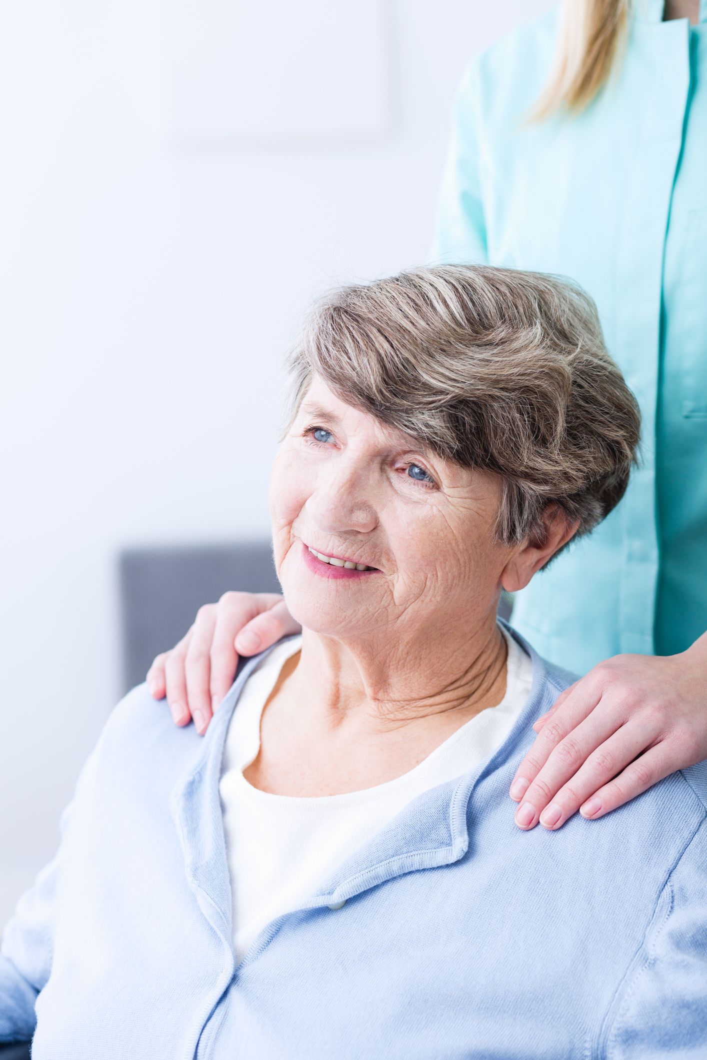 Elderly person with hands on shoulders, smiling, next to person in teal scrubs.