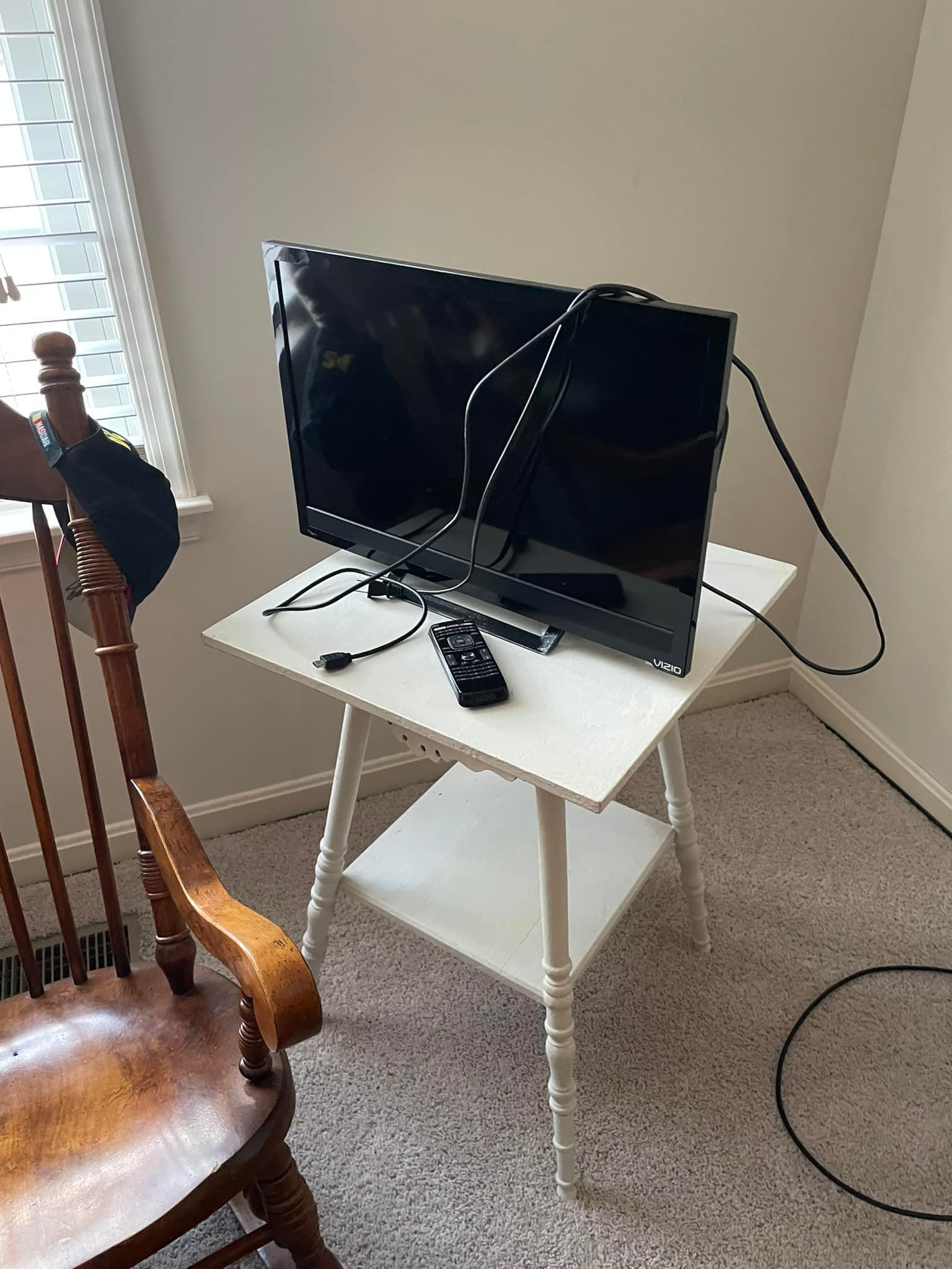 a flat screen tv is sitting on a white table next to a wooden chair .