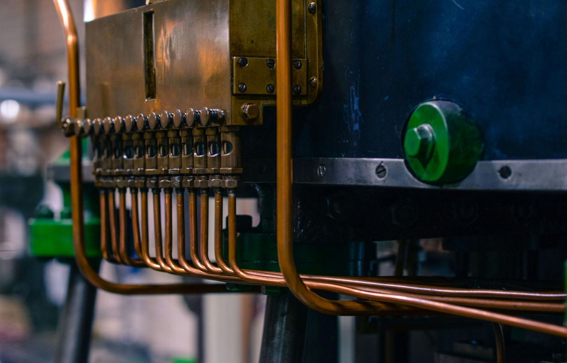 Close-up of a metallic industrial machine featuring a horizontal row of vertical copper tubes connected to a brass block.
