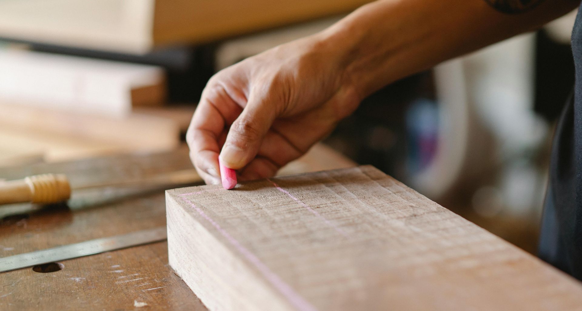 A person uses a pink chalk piece to mark a line on a piece of wooden lumber in a workshop.