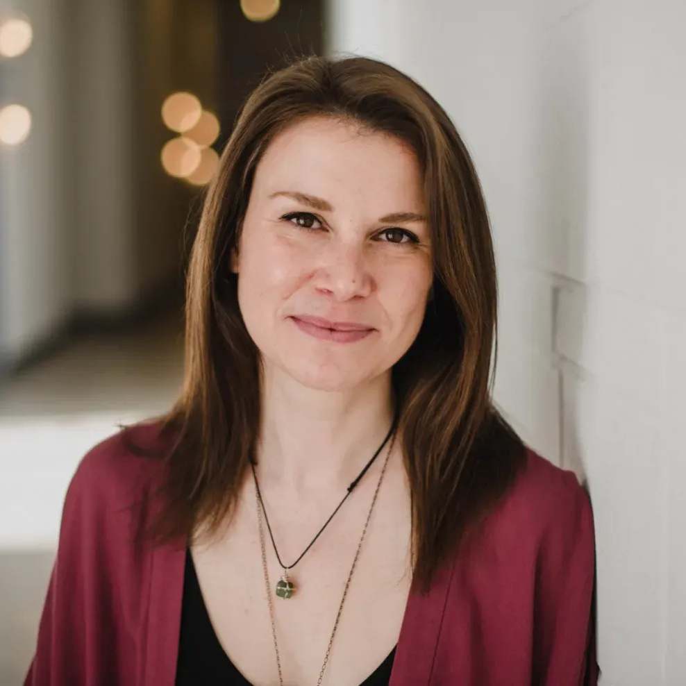 Woman in a burgundy top smiling in a softly lit indoor hallway