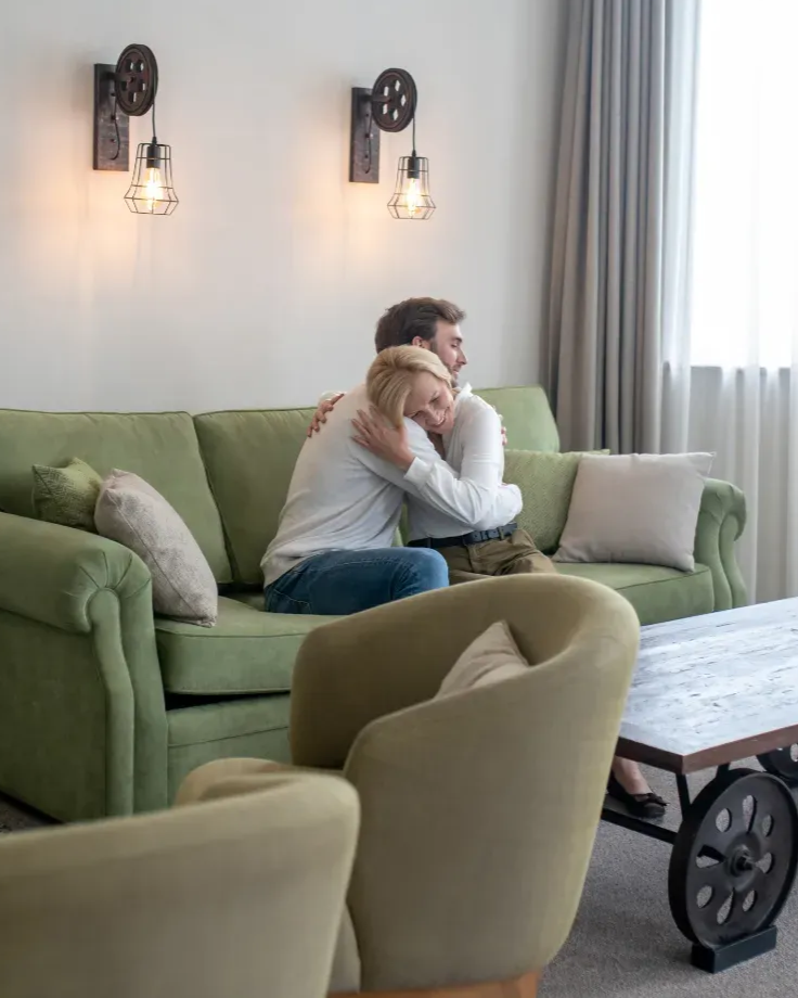 A lady sitting on a couch with hands on her laps.