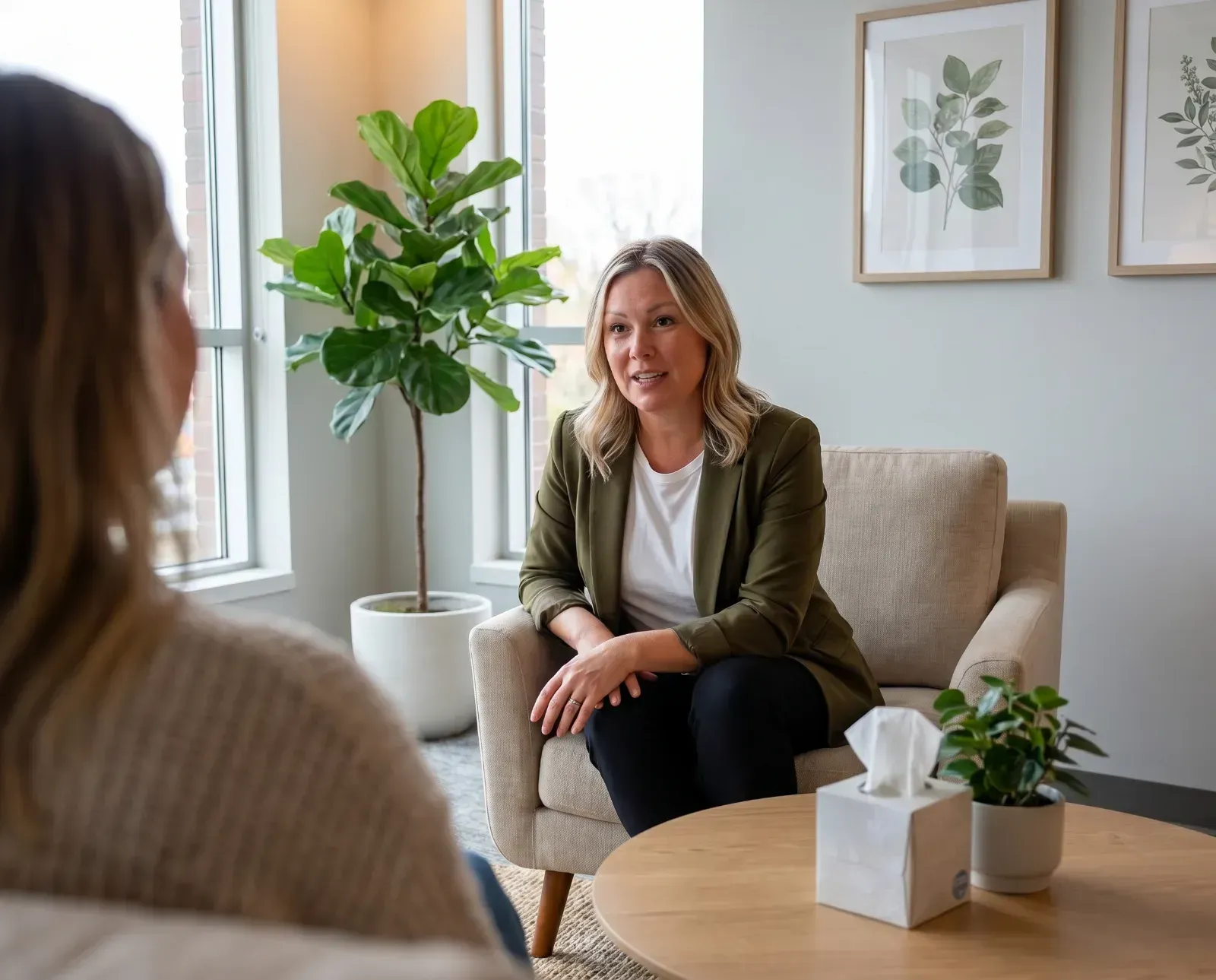 Counselor speaking with a client in a bright, modern office with plants and framed wall art