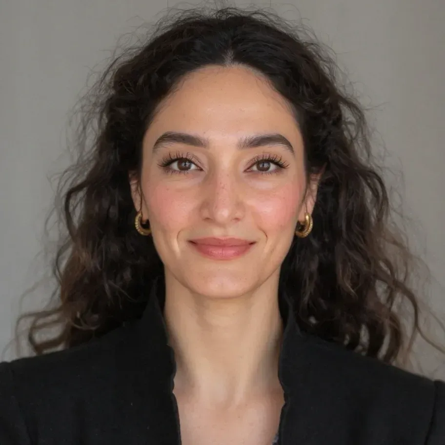 Portrait of a smiling woman with curly dark hair wearing a black blazer against a gray background