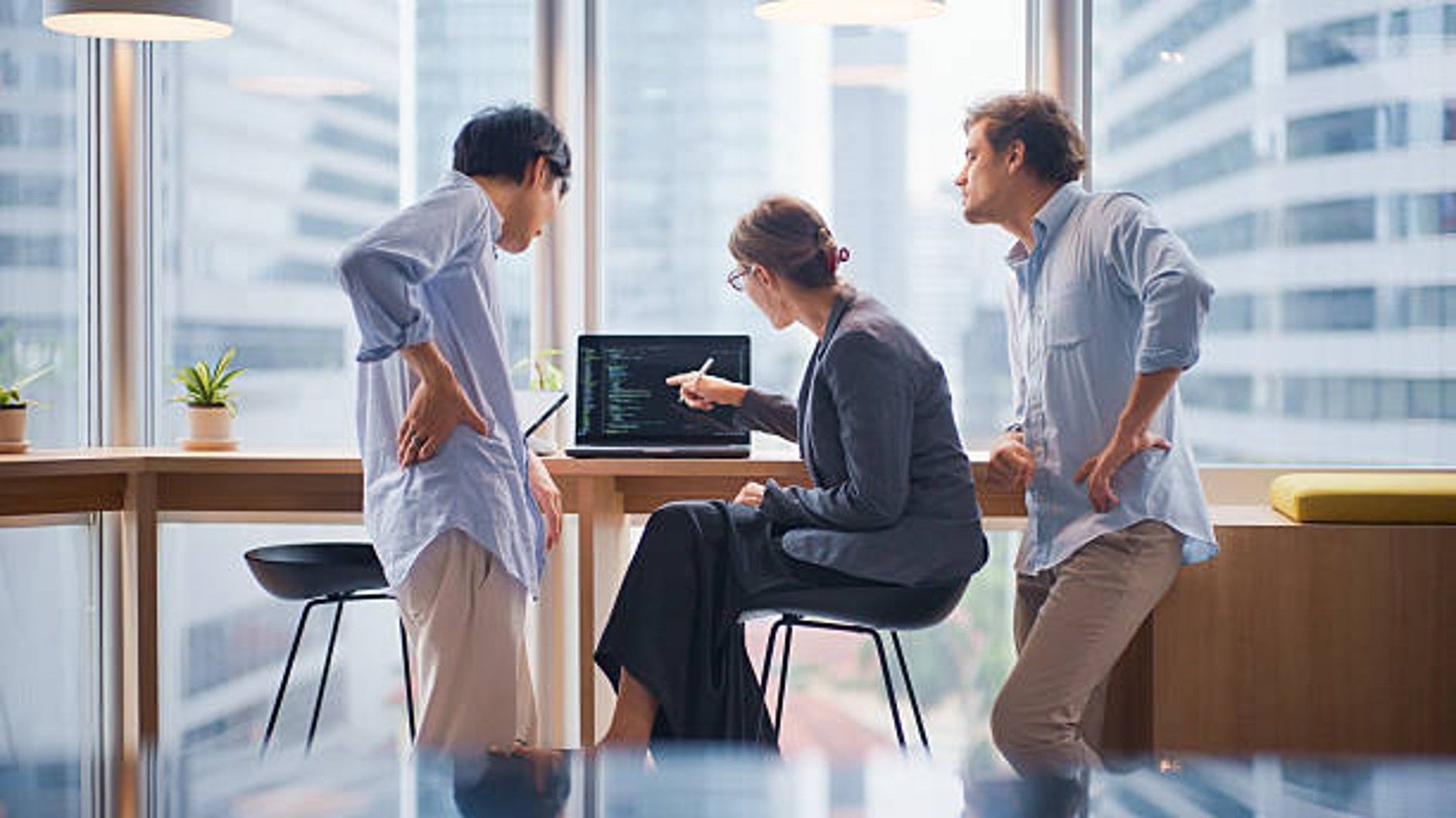 Two men and a woman working in an office, pointing at laptop.