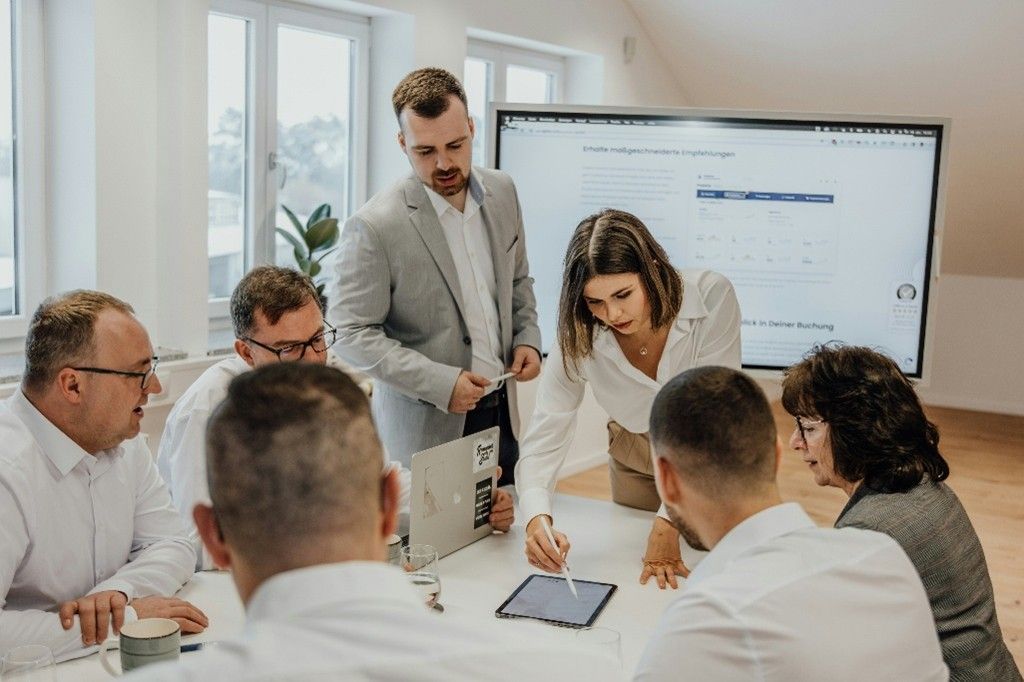Business team meeting around a table, reviewing a project displayed on a screen.