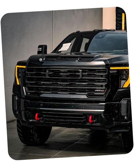 A black GMC Sierra AT4 pickup truck, viewed from the front, featuring distinct yellow headlights and red tow hooks. | Dierks Diesel & Auto Performance
