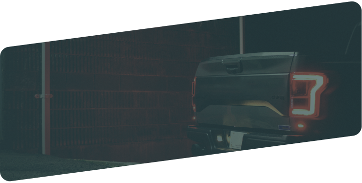 The rear view of a dark pickup truck with its illuminated C-shaped taillight at night. | Diesel & Auto Performance