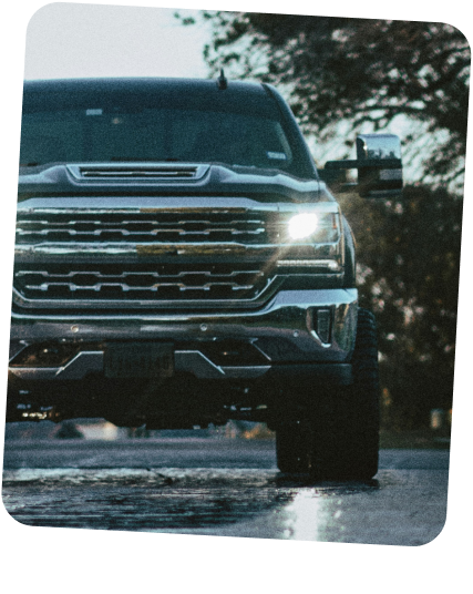 A dark pickup truck with chrome accents and bright headlights drives on a wet road. | Dierks Diesel & Auto Performance