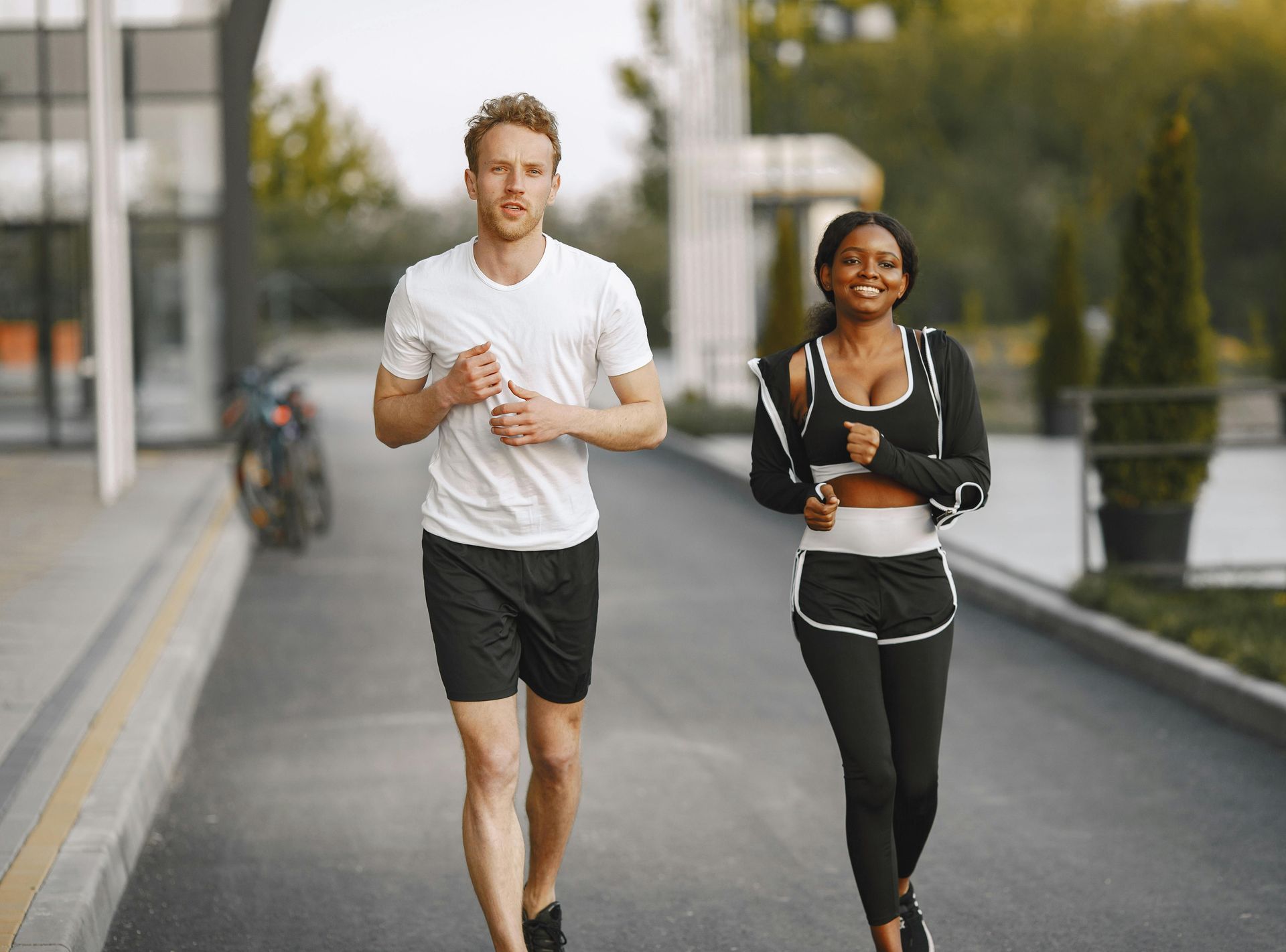 Two people in athletic wear jogging on an outdoor paved path near a building.
