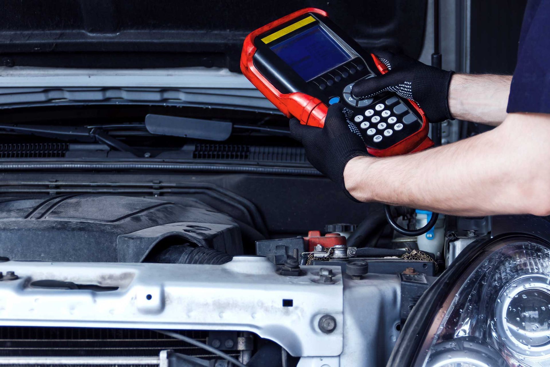Mechanic using a red diagnostic scanner under a car hood