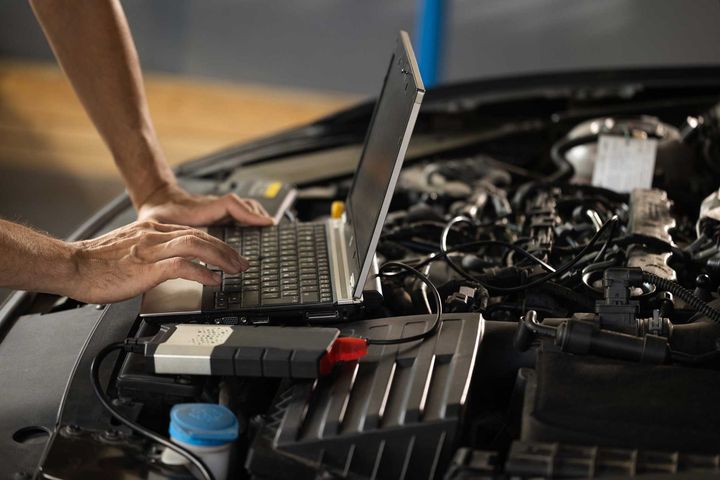 Person using a laptop to diagnose a car engine in an open hood compartment