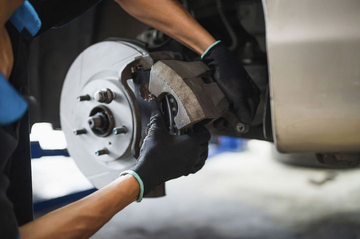 Mechanic replacing a car brake rotor with gloved hands