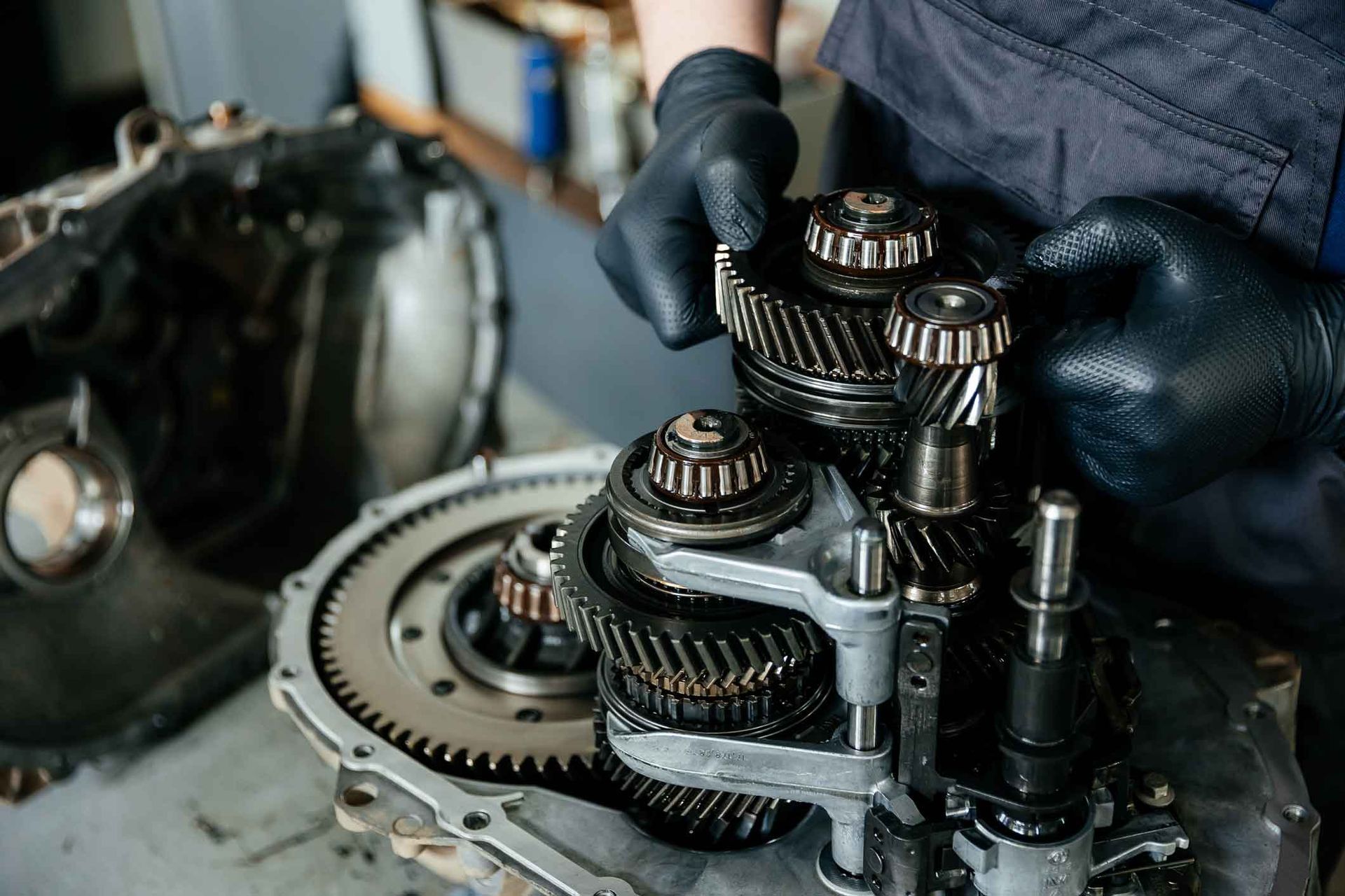 Mechanic’s gloved hands repairing a metal gearbox with exposed gears and parts