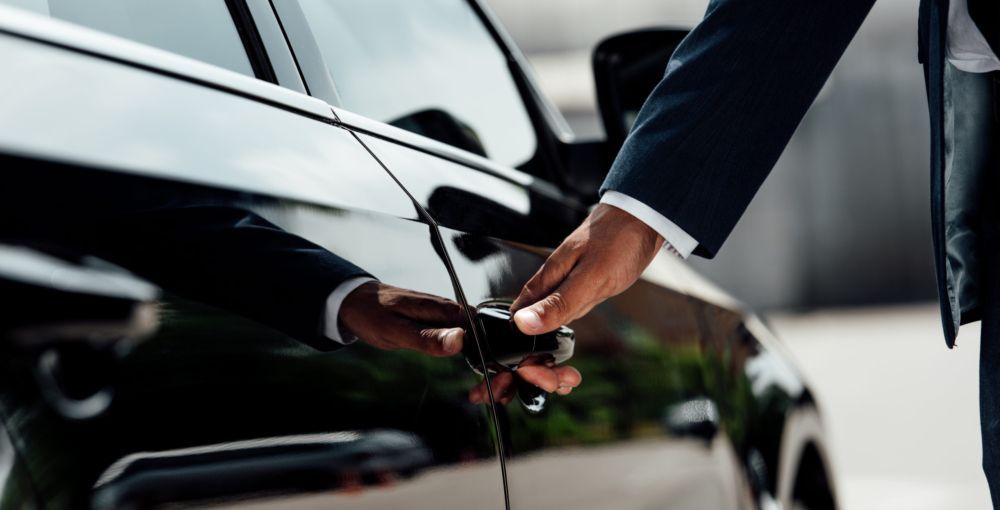 A man in a suit is opening the door of a black car.