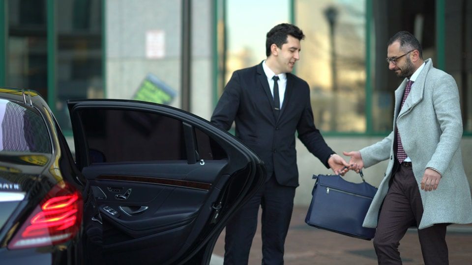 A man in a suit is helping another man get out of a car.