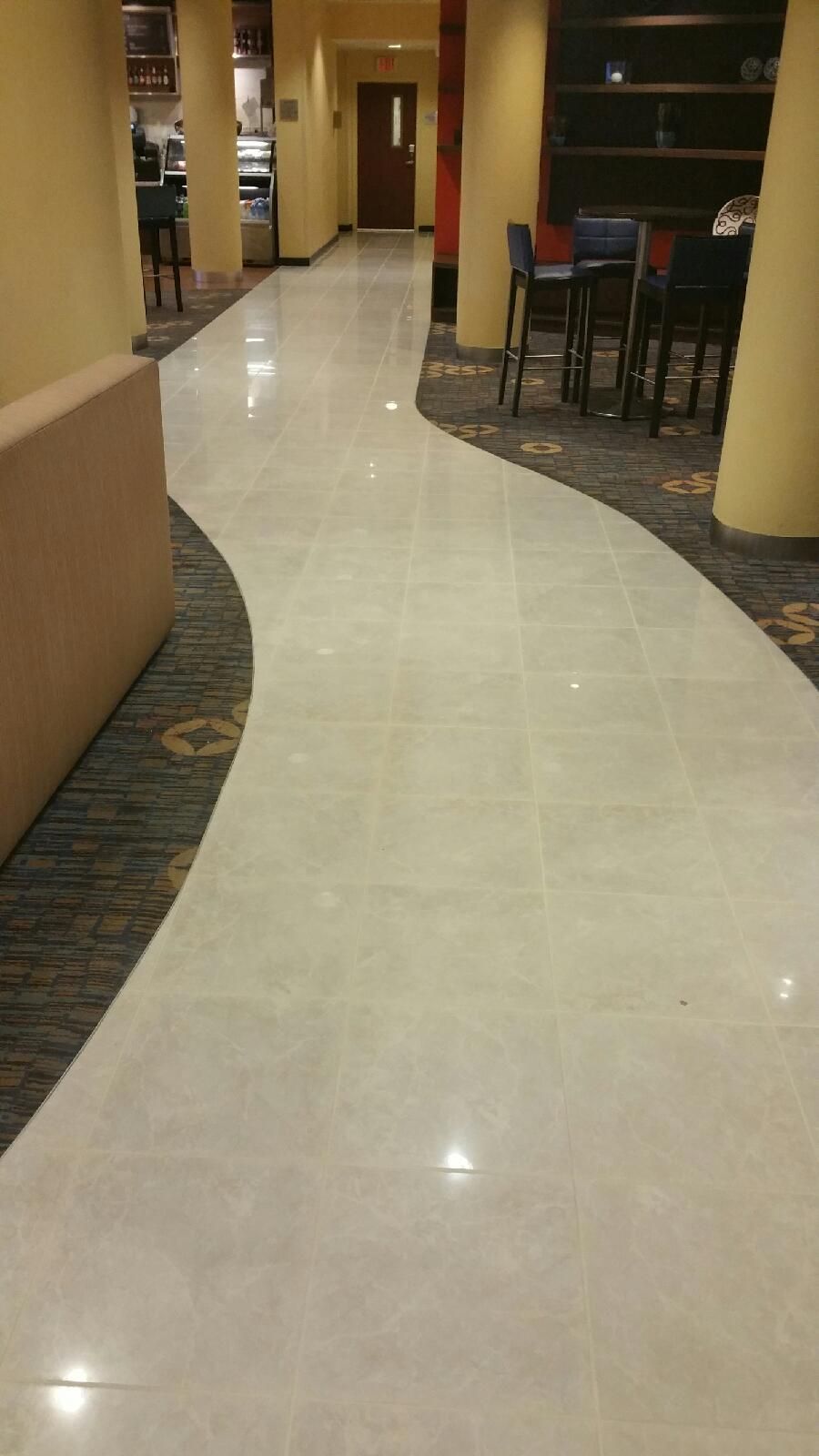 Hallway with a curved, light-colored tile path bordered by carpet. Tables and a sofa line the sides.