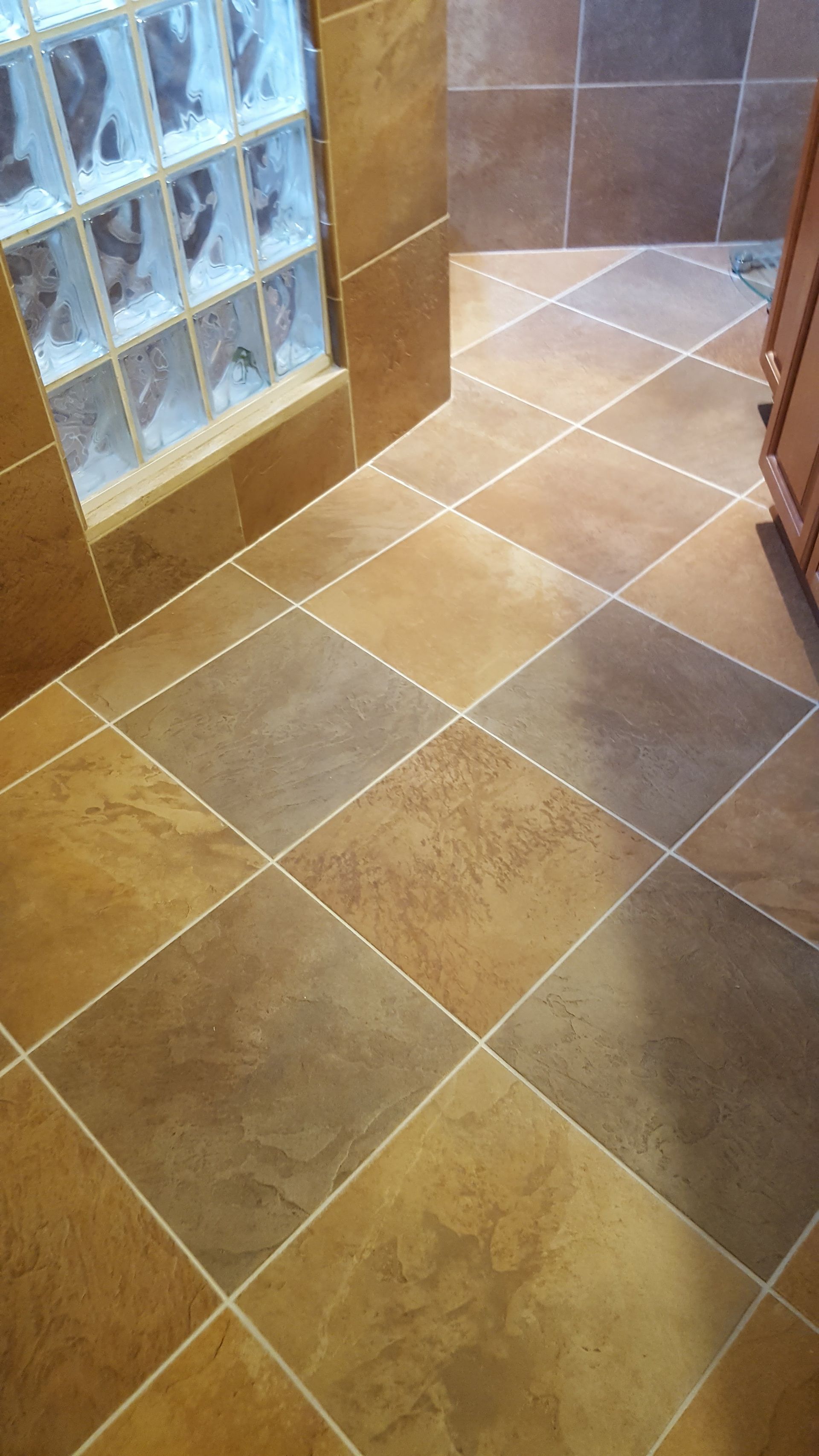 Brown tiled bathroom floor with square pattern, by a glass block window.
