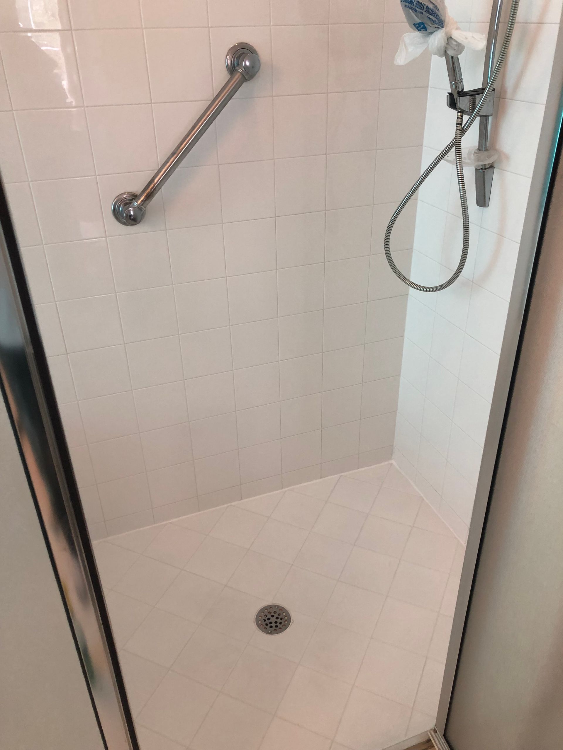 White tiled shower with grab bar and showerhead.