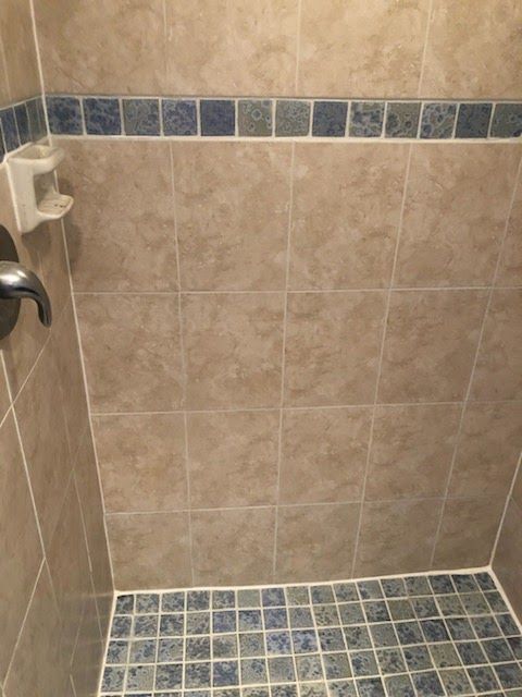 Beige tiled shower with blue and white mosaic accent tiles. White soap dish attached to the wall.