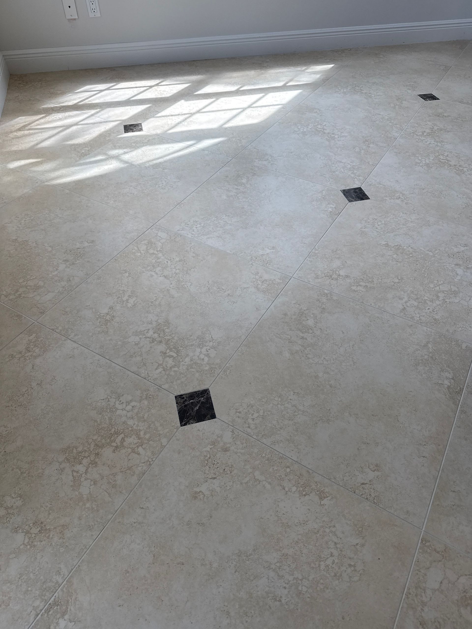 Beige tile floor with scattered black square insets. Sunlight streams across the tiles from a window.
