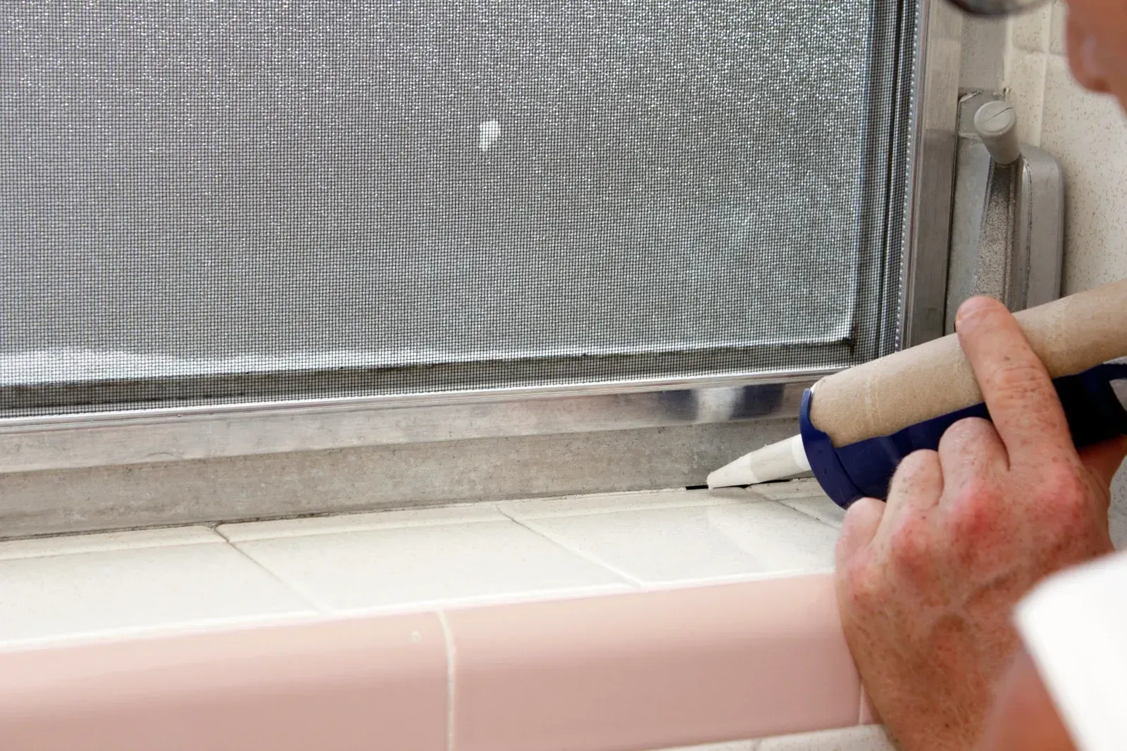 Person sealing a window frame with white caulk.