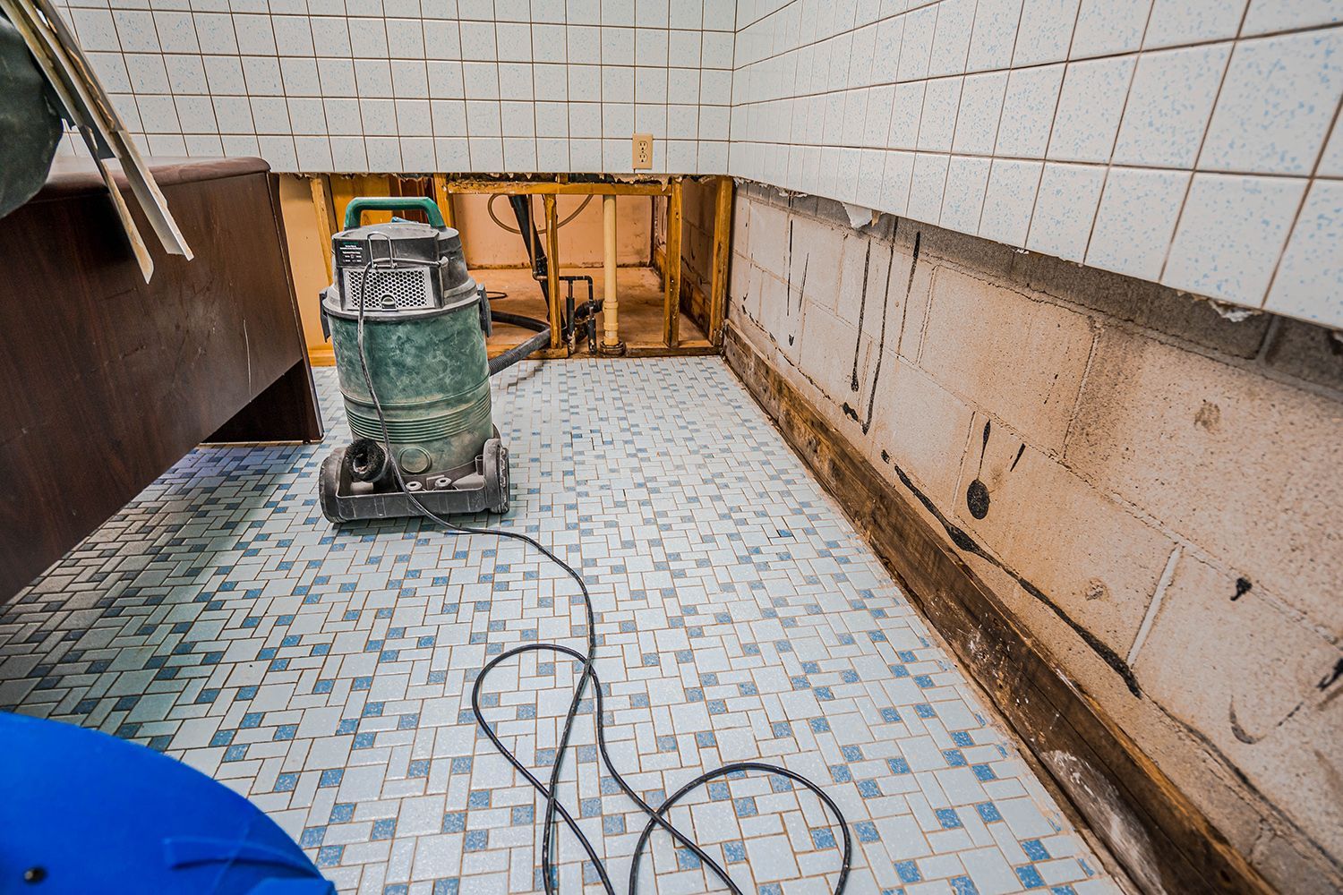 A bathroom featuring a green vacuum cleaner positioned on the floor to clean up flooding.