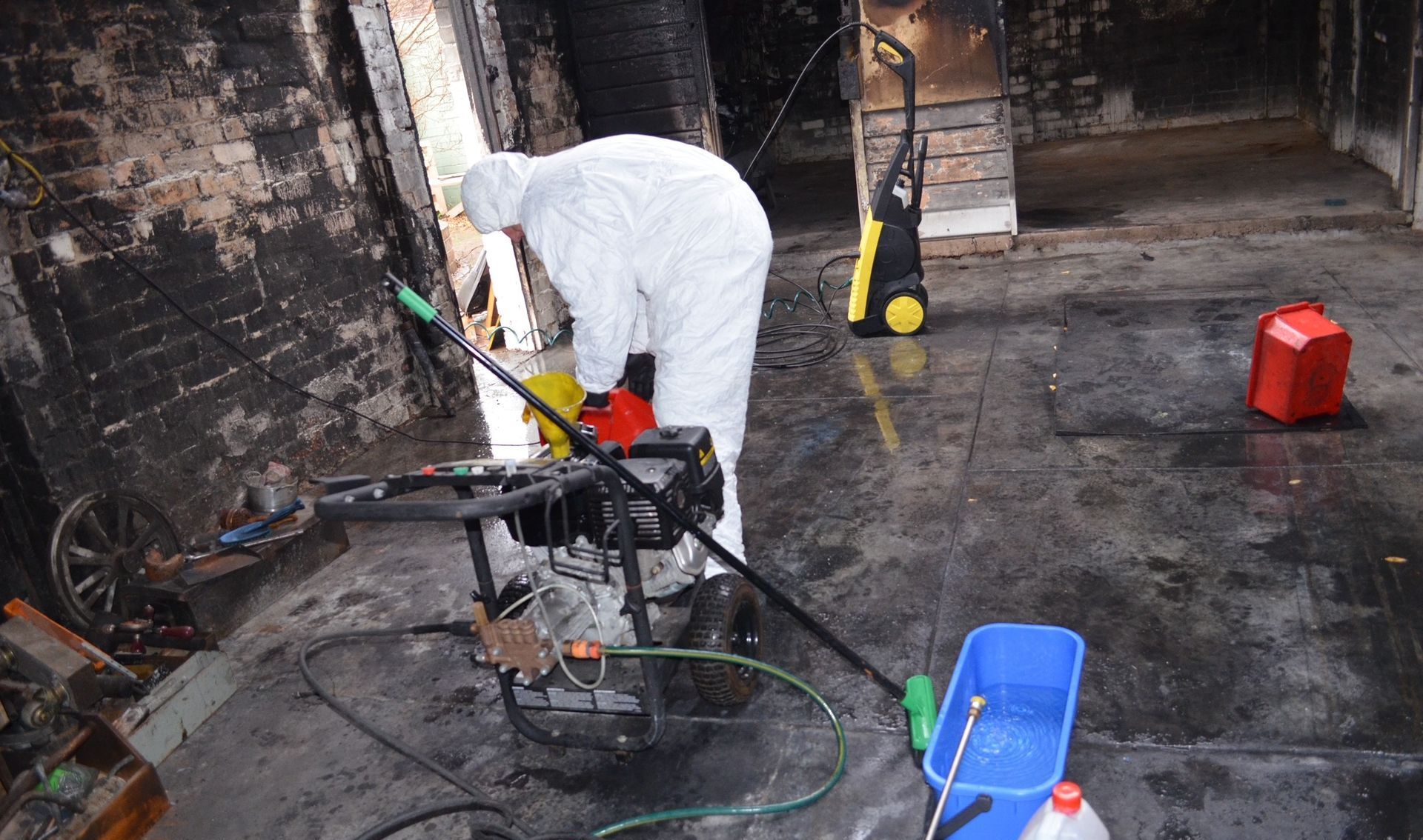A man in a protective suit is cleaning a machine with a high pressure washer.