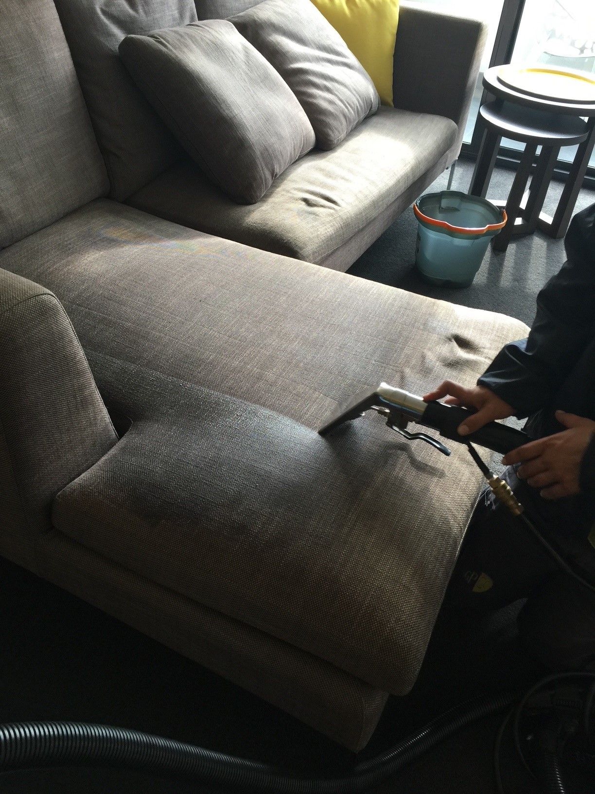 A person wearing pink gloves is cleaning a couch with a vacuum cleaner.