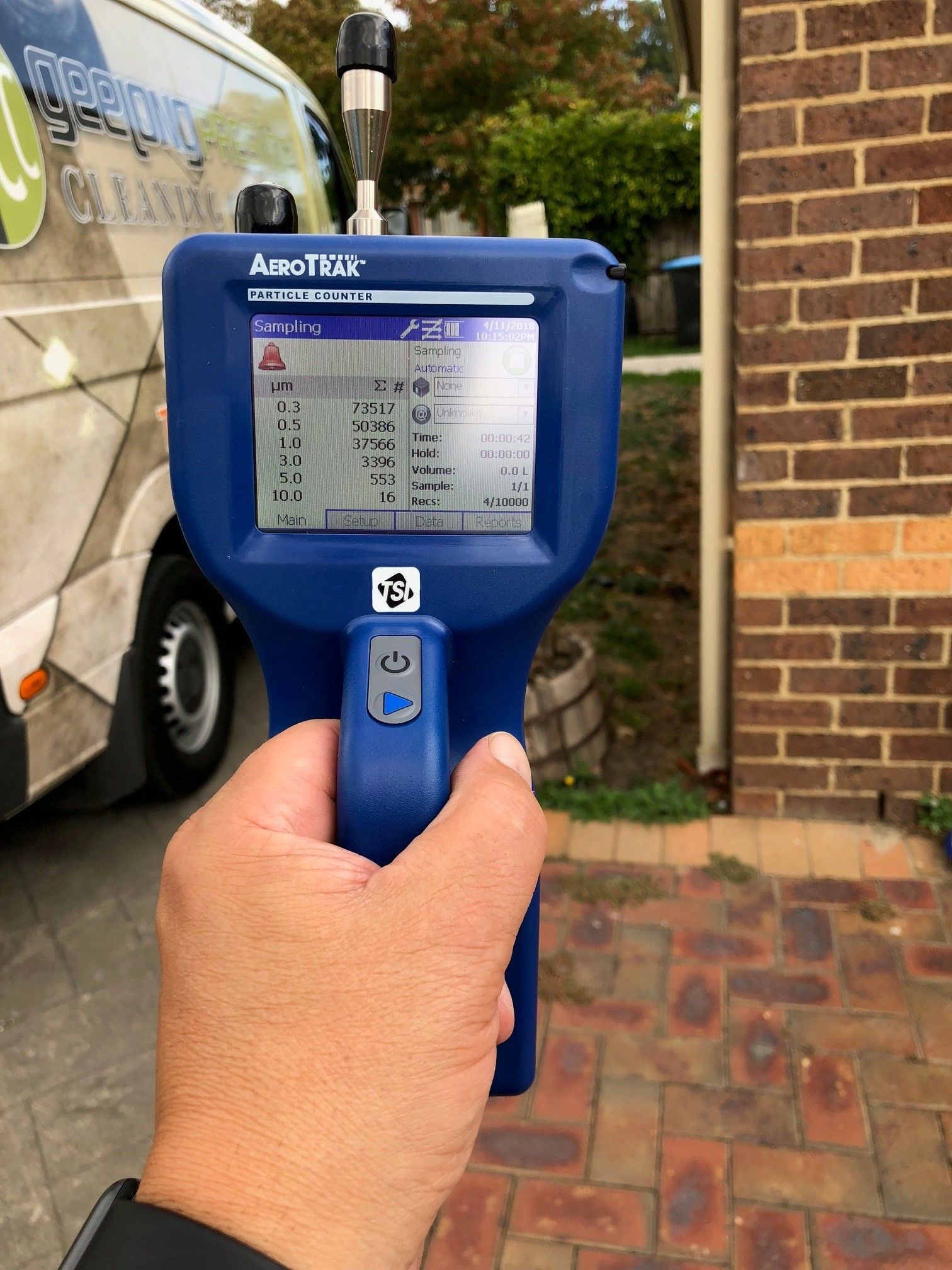 A person is holding a device in front of a brick building.