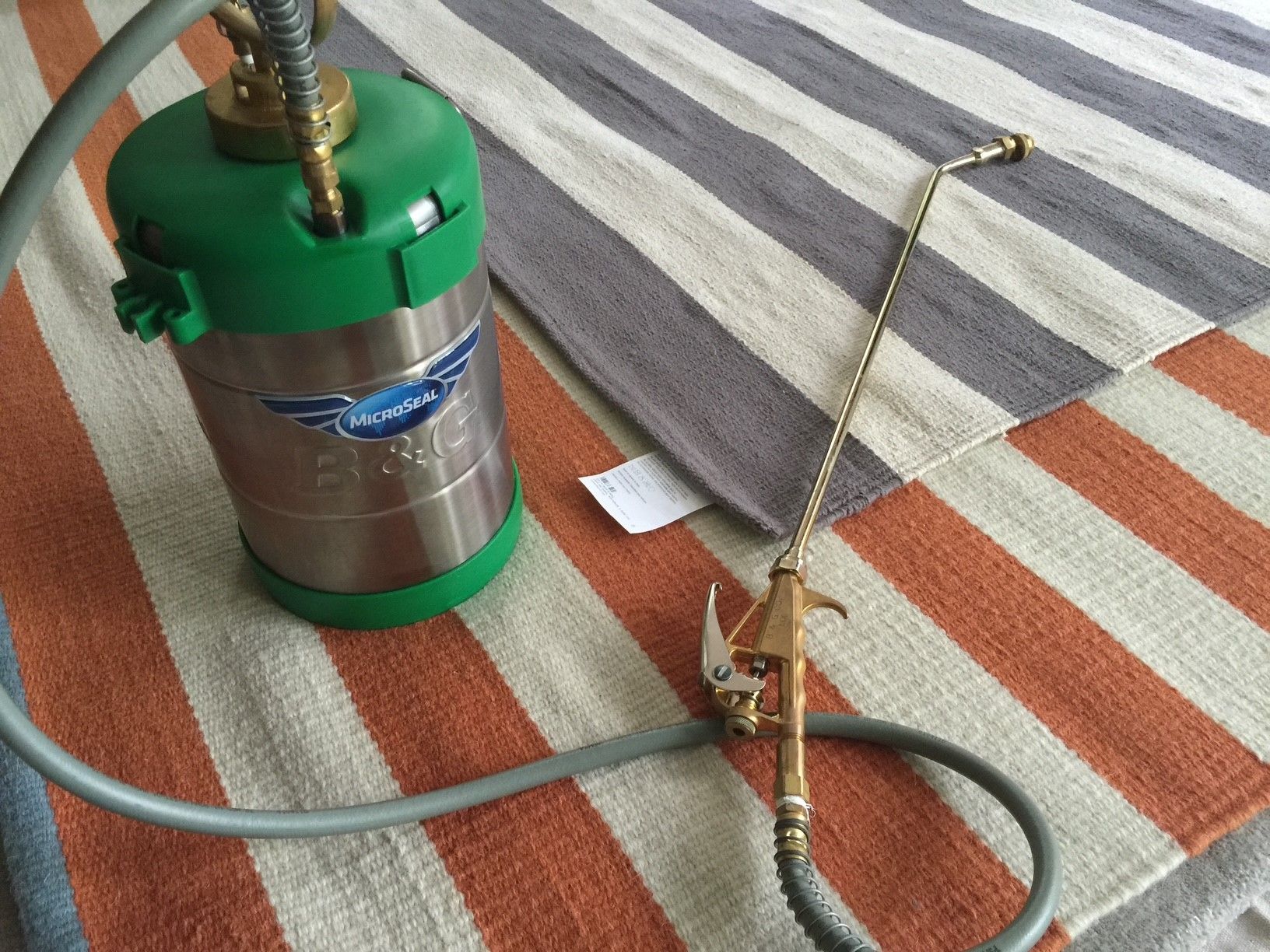 A stainless steel sprayer is sitting on a striped rug