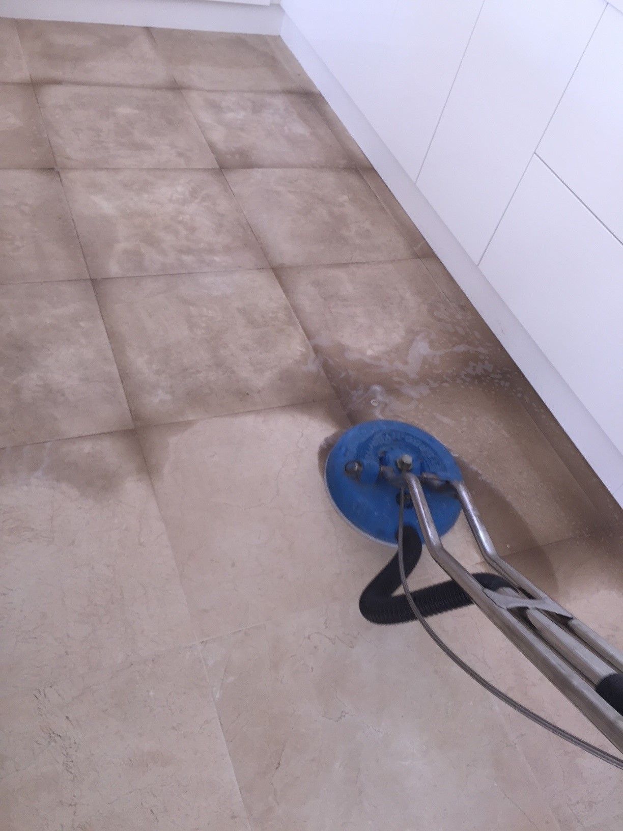 A person is cleaning a tile floor with a vacuum cleaner.