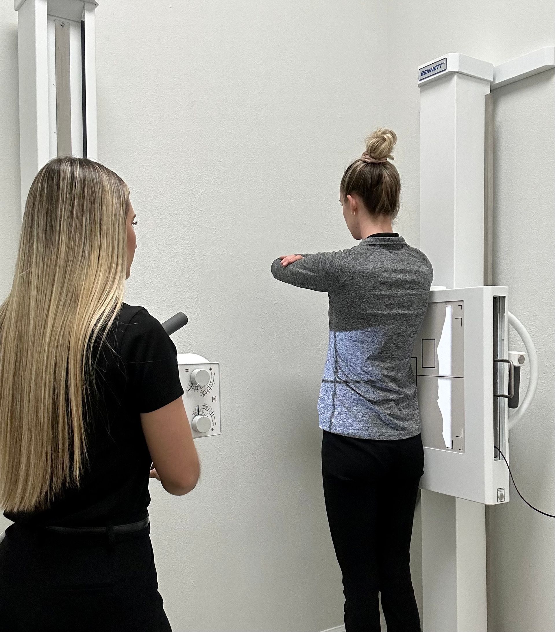 Two women are standing in front of an x-ray machine.
