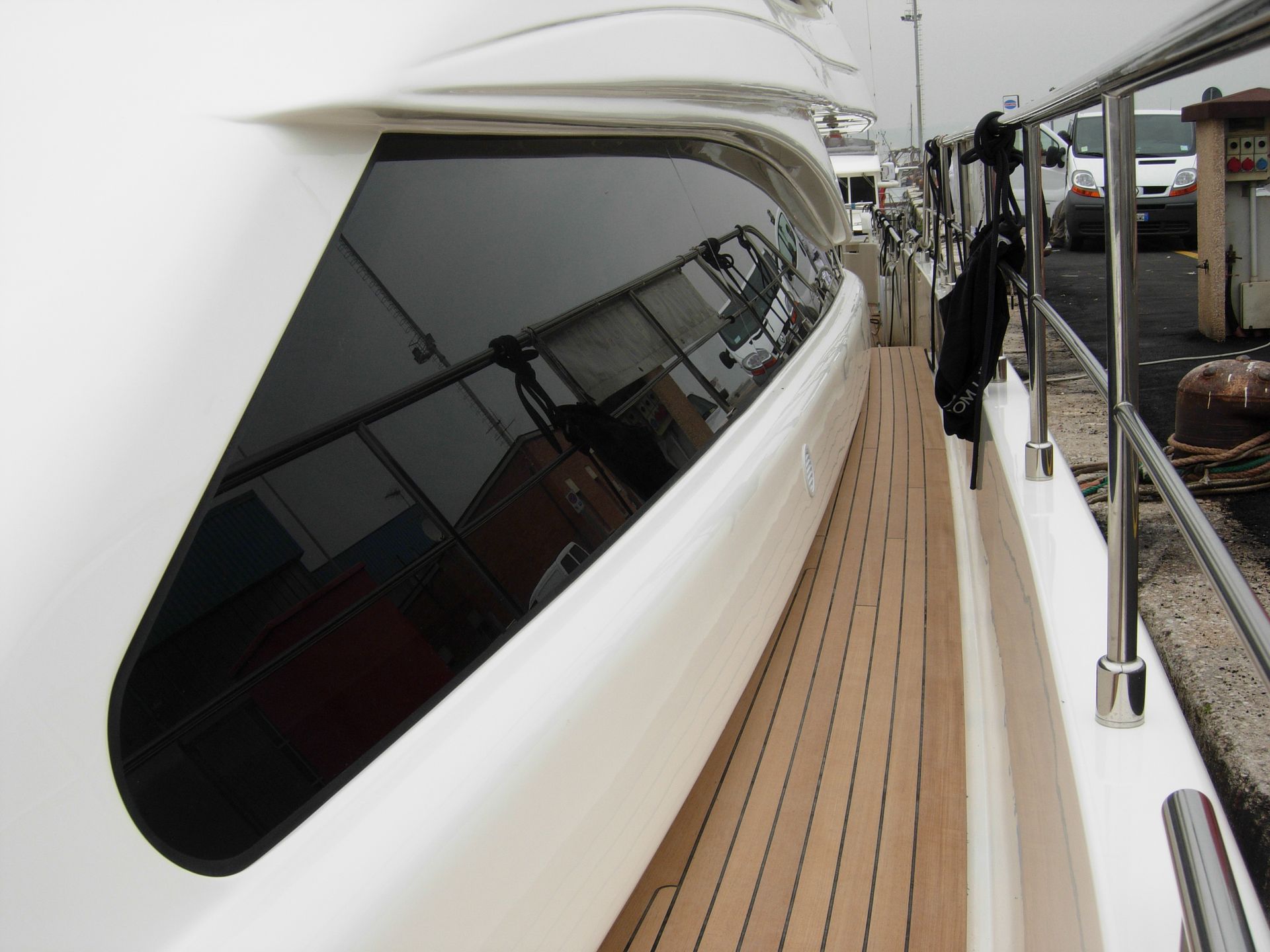 Primo piano della fiancata di uno yacht di lusso. Mostra una finestra scura, un ponte in legno e ringhiere in acciaio.
