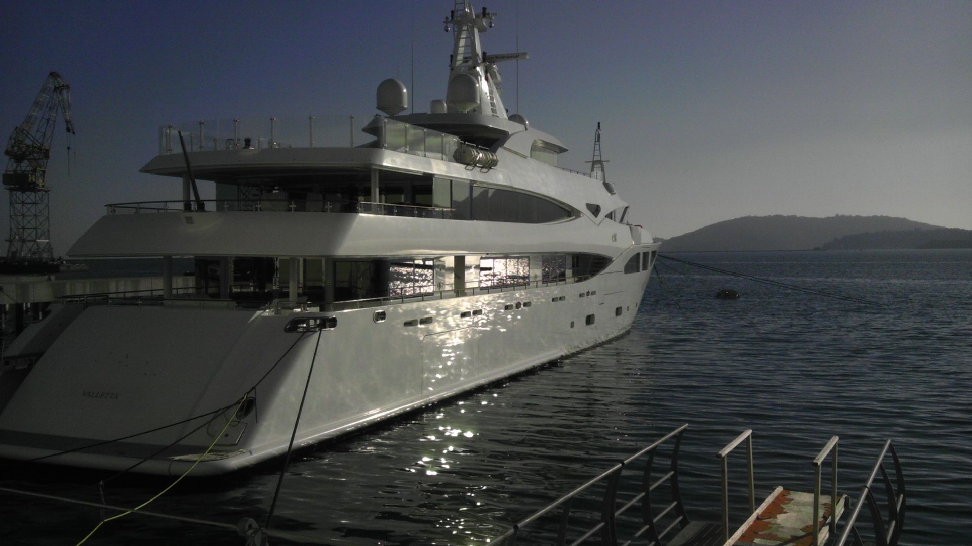 Un grande yacht bianco attraccato a un molo riflette la luce del sole sull'acqua.