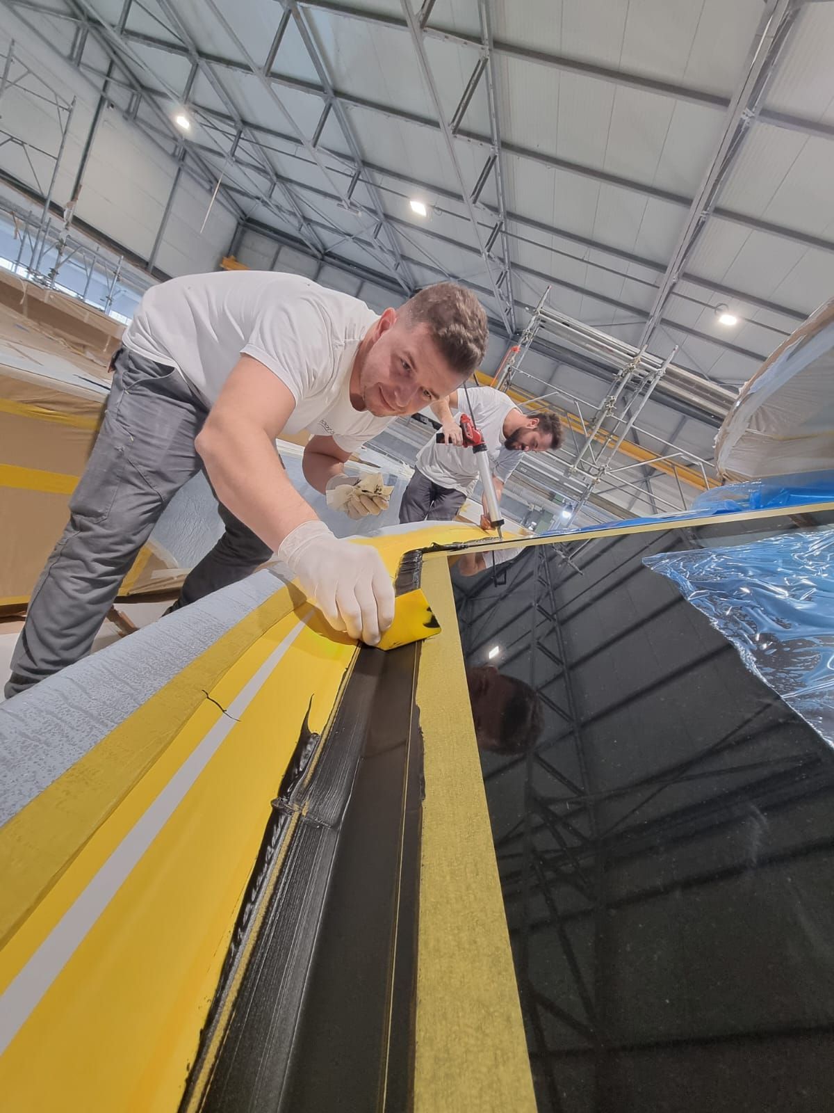 Un grande telaio di finestra sollevato da una gru a ponte all'interno di uno stabilimento di produzione di imbarcazioni.