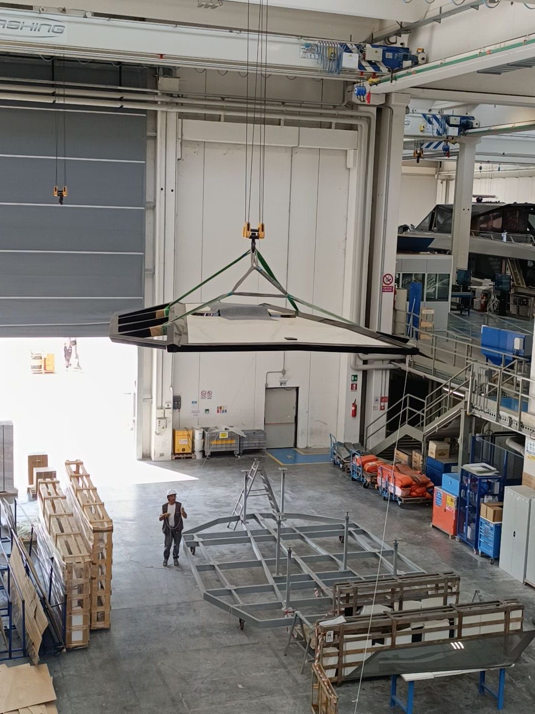 Un grande pannello sospeso da una gru in un magazzino; sotto c'è una persona.