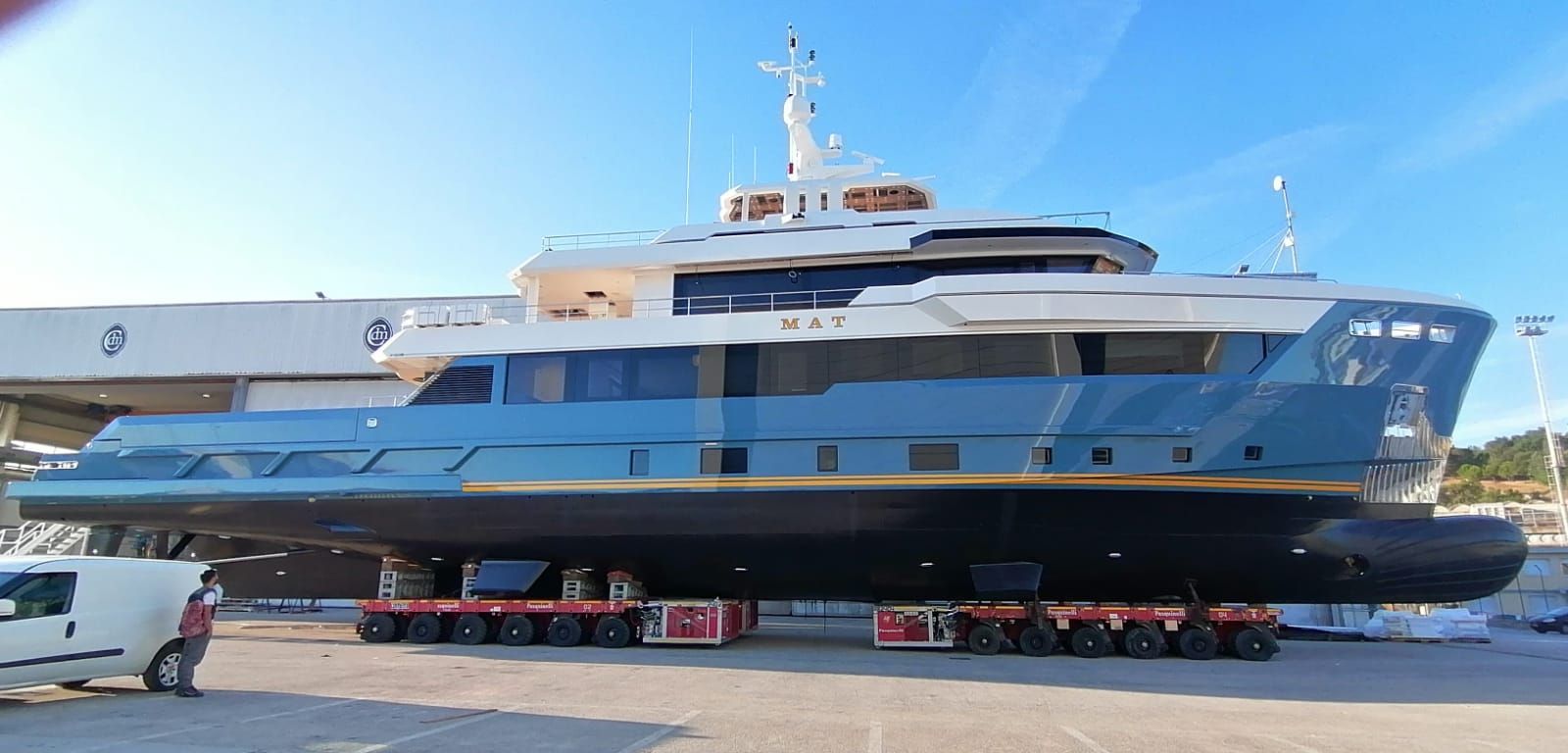 Un grande yacht blu su un rimorchio in un cantiere navale, sotto un cielo azzurro brillante.