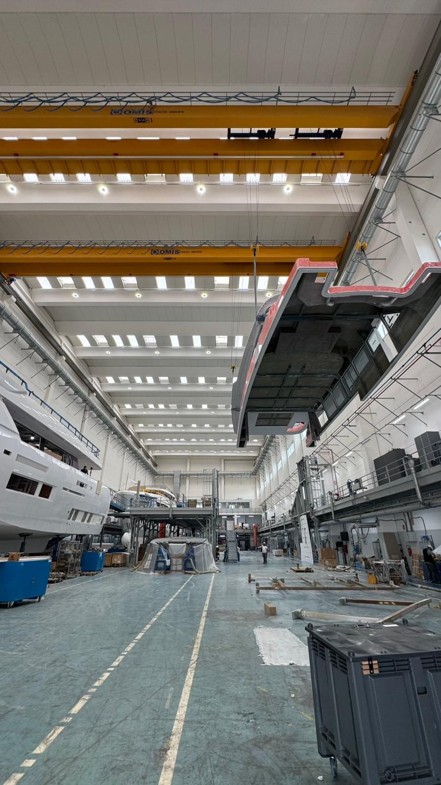 All'interno di una grande fabbrica, lo scafo di una barca è sospeso in aria. Sono visibili altre imbarcazioni in costruzione.