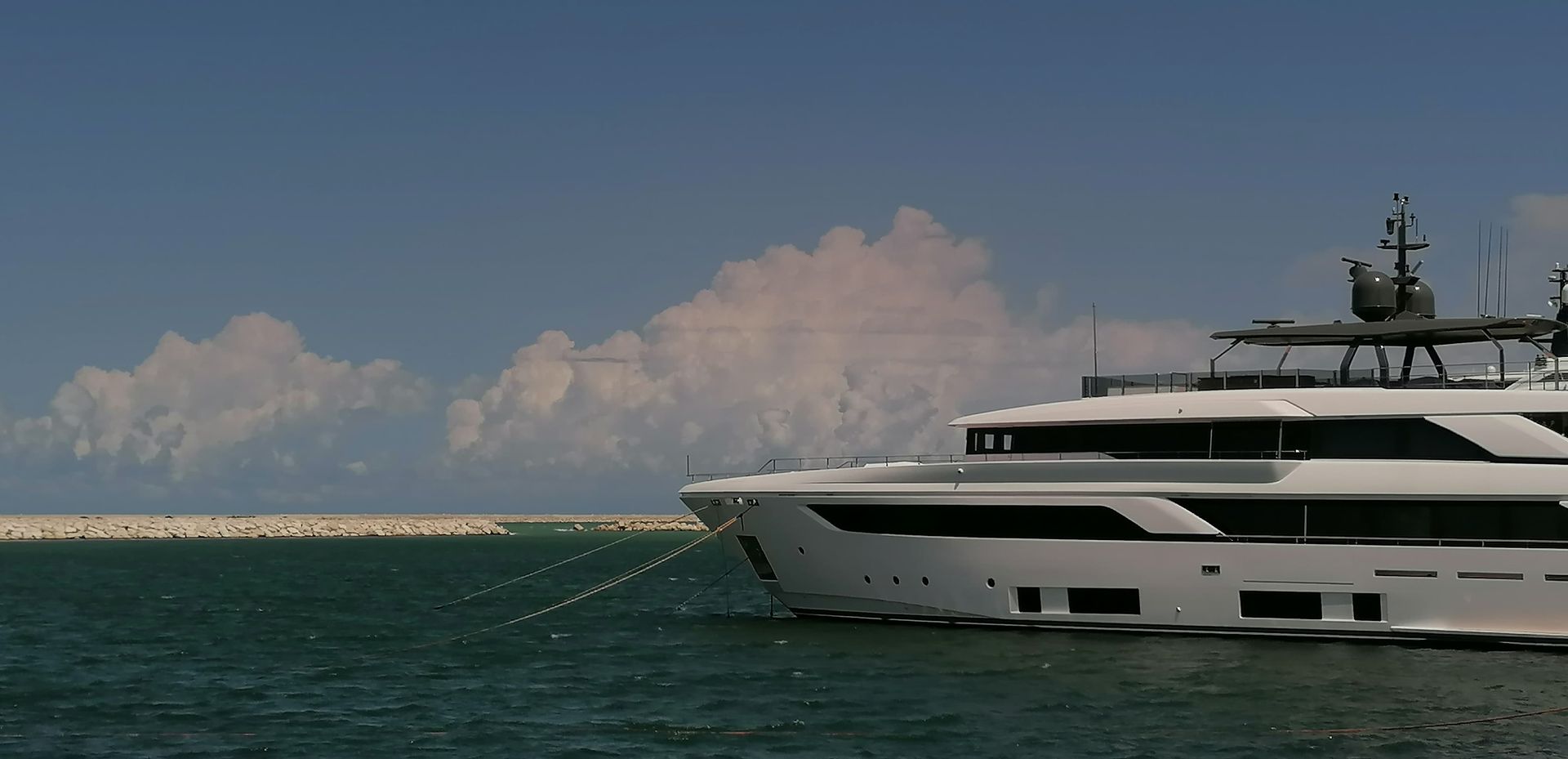 Un grande yacht bianco galleggia sull'acqua verde, con un cielo azzurro e nuvole sullo sfondo.