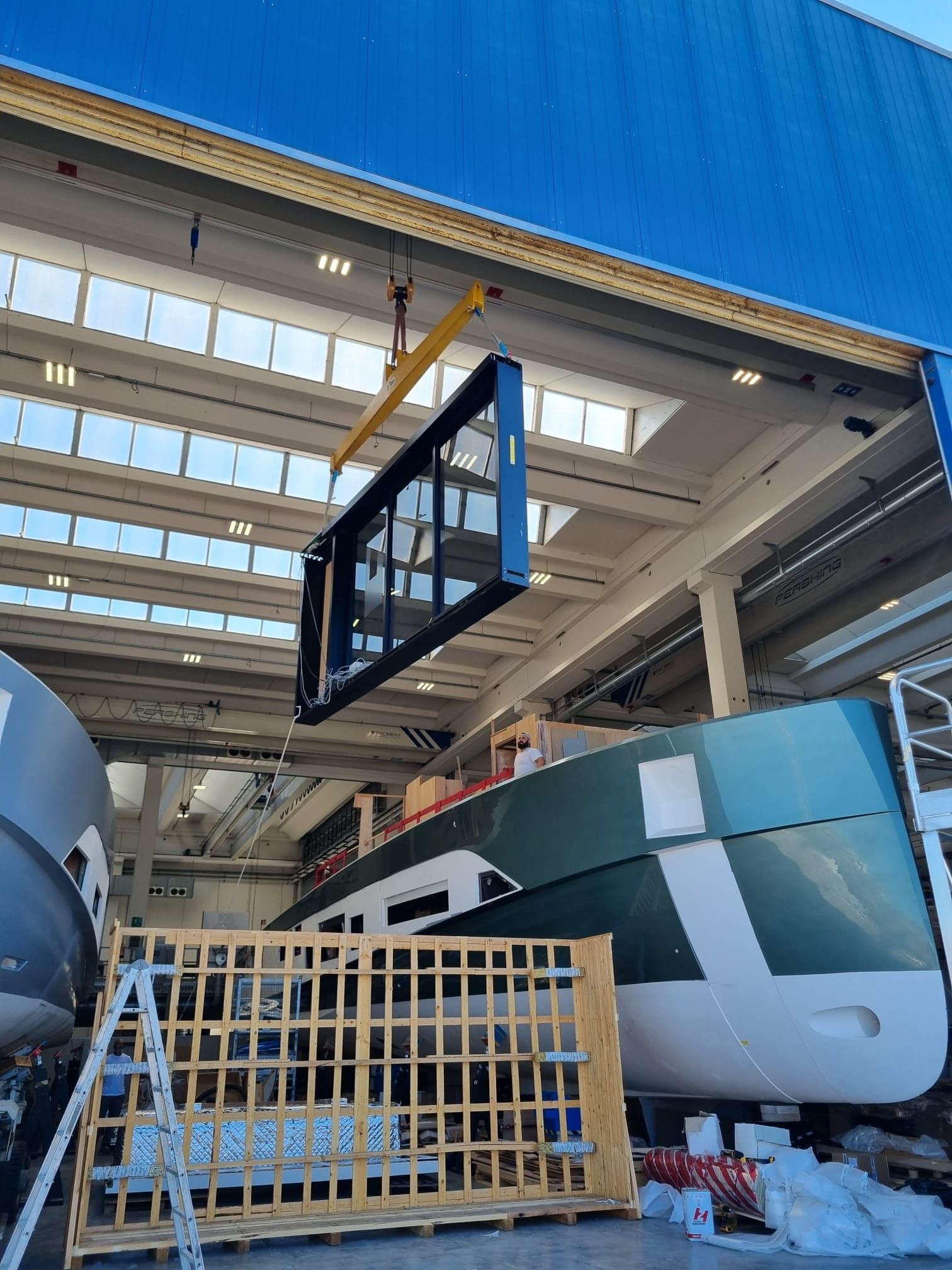 Un grande telaio di finestra sollevato da una gru all'interno di un magazzino di produzione di imbarcazioni.