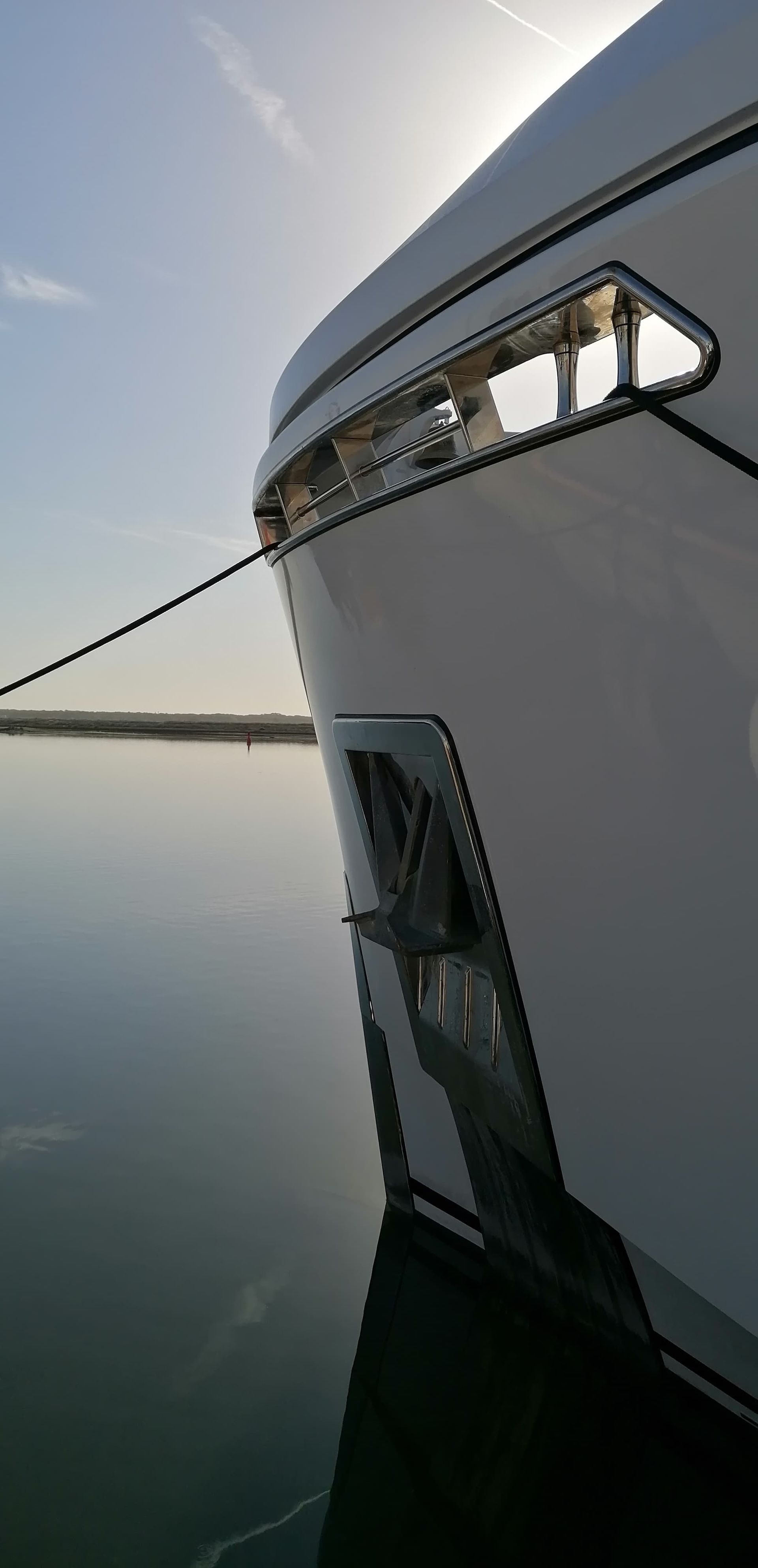 La prua di una barca bianca è ormeggiata a un molo, con vista sull'acqua e sul cielo.
