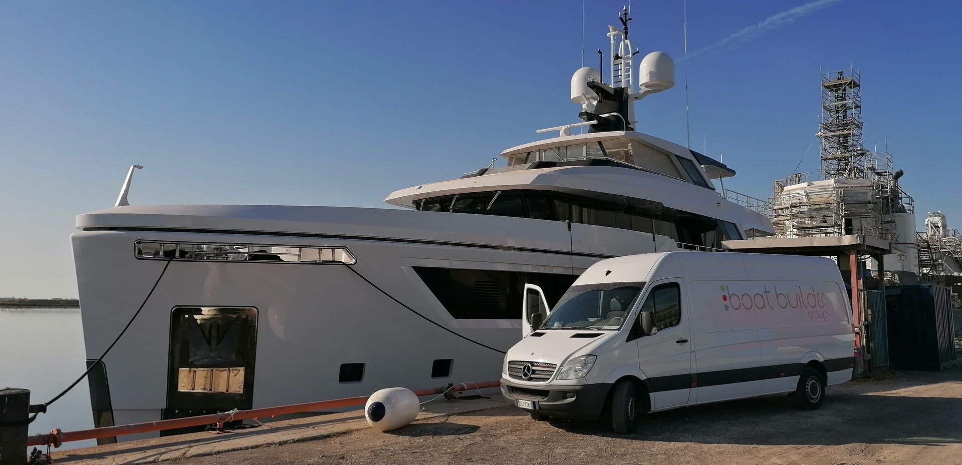Un grande yacht bianco attraccato accanto a un furgone di servizio bianco in una giornata di sole.