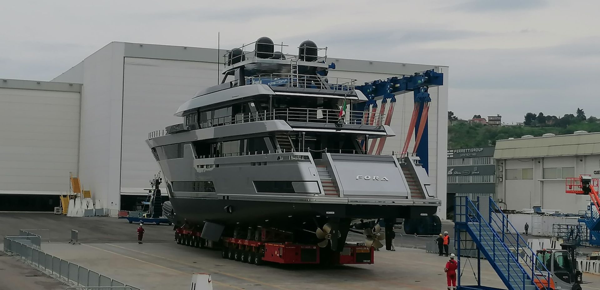 Un grande yacht viene trasportato fuori da un edificio su una piattaforma con ruote.